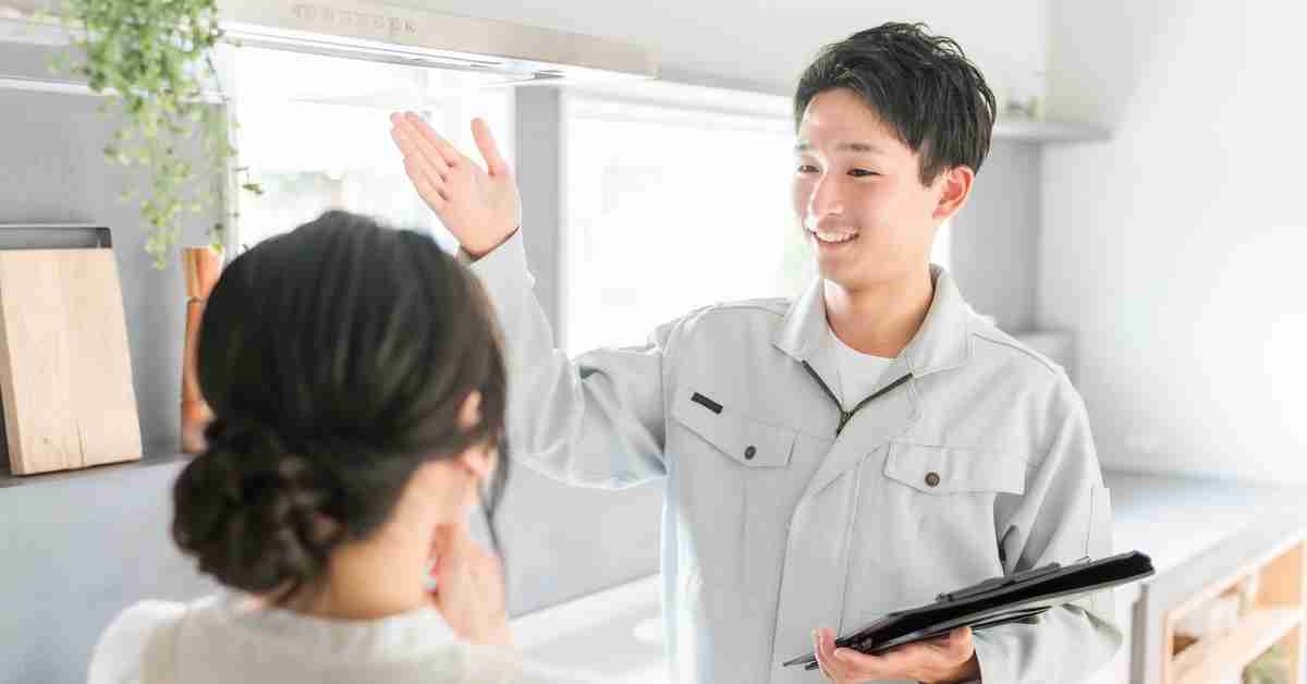 A man and a woman standing in a room. He is holding a binder and gesturing while she watches him.