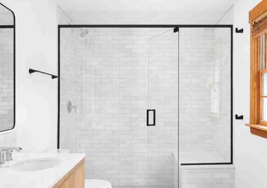 A luxury walk-in shower with white tile, glass doors, and black trim in a clean, white bathroom.