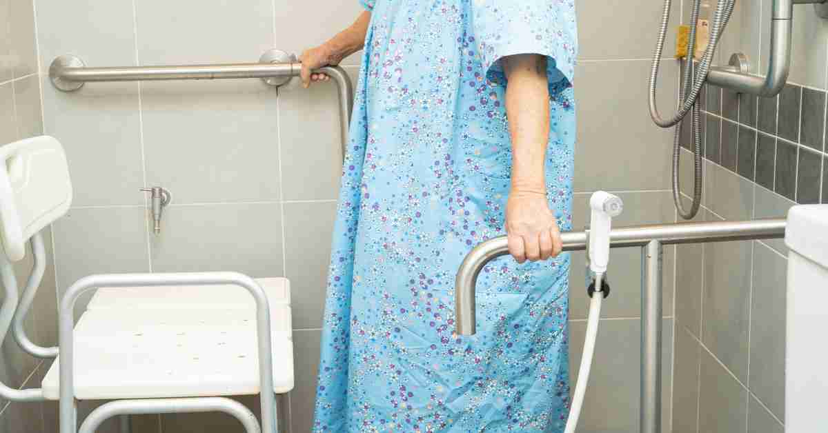 A person standing in a walk-in shower, holding onto two grab bars. There is also a white chair in the shower.