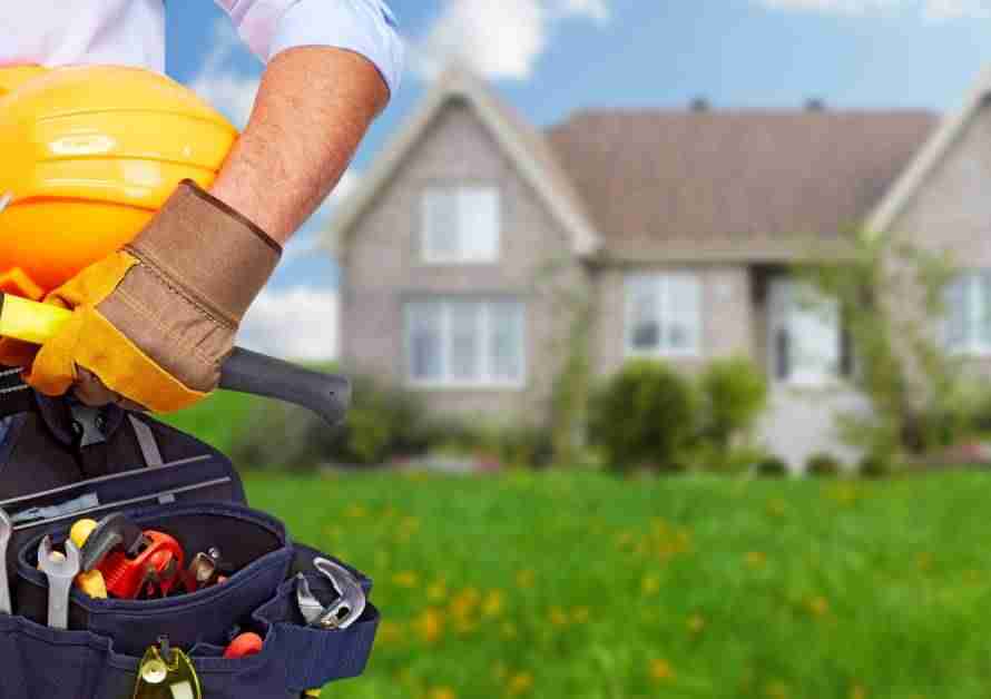 A construction worker with a tool belt and a hard hat stands in the front yard of a house.