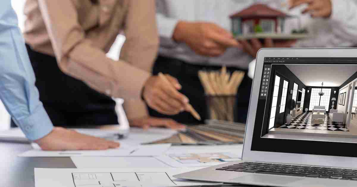 A group of people work around a table full of floor plans. In front of them is a laptop with a digital illustration of a room.