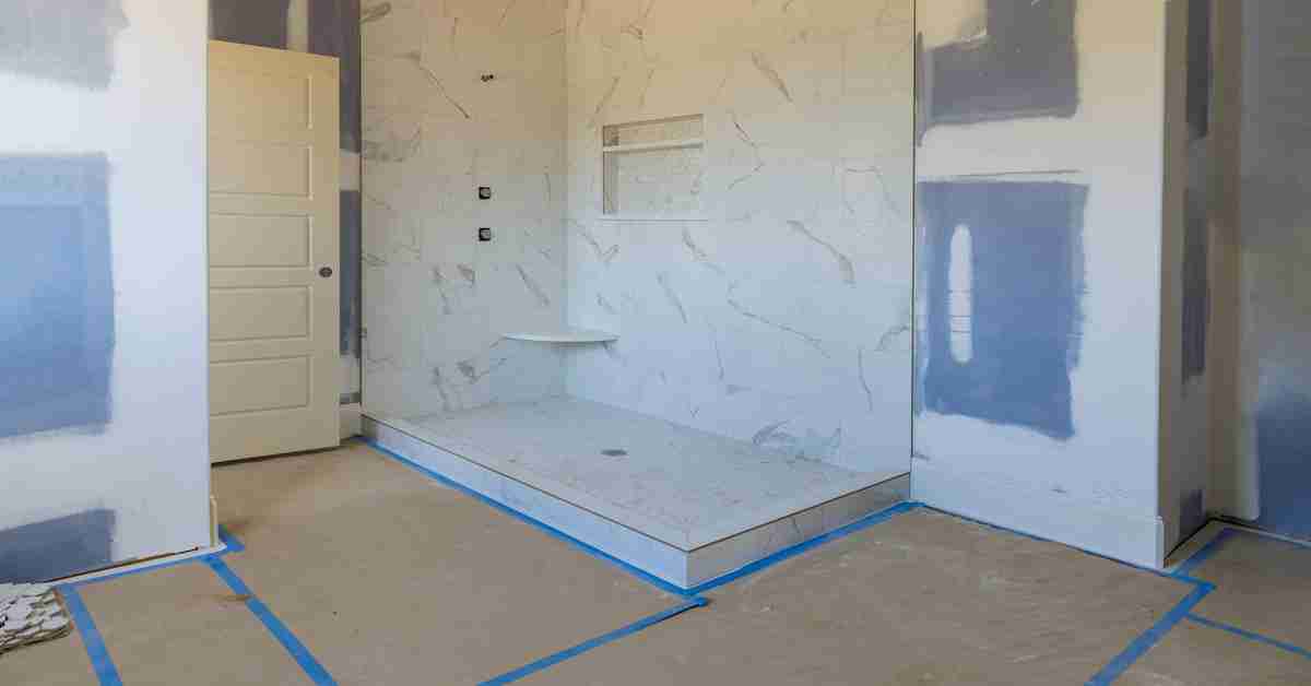 A bathroom in the middle of renovation. There is tape on the ground and a partially finished walk-in shower.