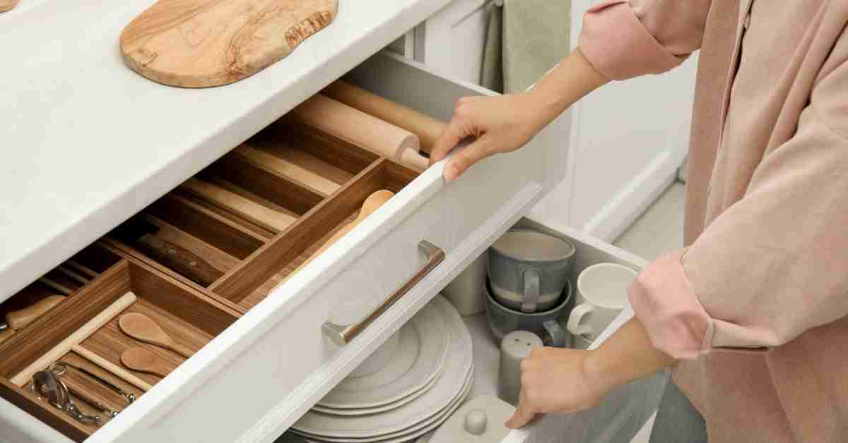 A person wearing a pink shirt opening two white drawers in a residential kitchen. Each drawer has shiny silver handles.