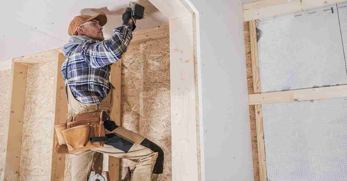 A contractor in a partially finished living space. They are using a drill to make a hole in the ceiling.