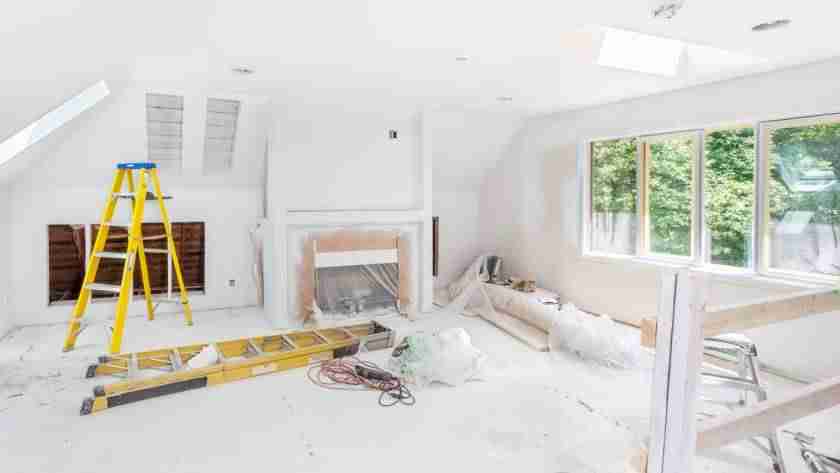 A living room that is currently being remodeled. The room is full of construction equipment, including two ladders.